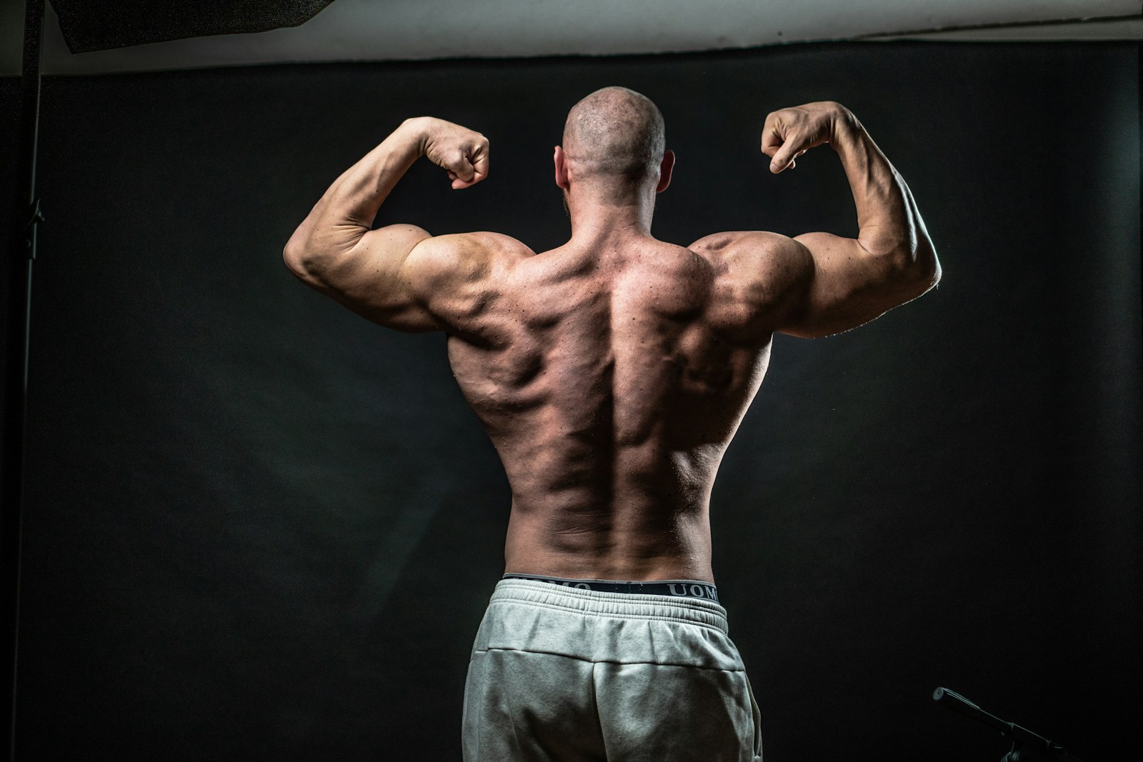 黒い背景の前でバックダブルバイセップスのポーズをとる男性の後ろ姿